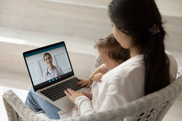 Loving young mother holding baby, making video call to pediatrician Loving mother hugging holding baby little daughter, using laptop, making video call to female pediatrician at home, doctor consulting caring mom online, telemedicine and children healthcare concept telemedicine stock pictures, royalty-free photos & images