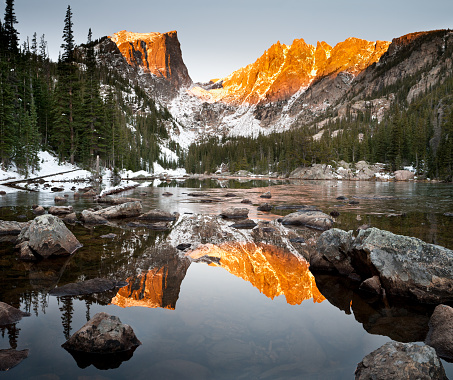 Sunrise on a calm October morning creates a warm alpenglow on Hallet Peak.  The still waters of Dream Lake reflect the mountains perfectly in the water.  Taken at Rocky Mountain National Park, Colorado.