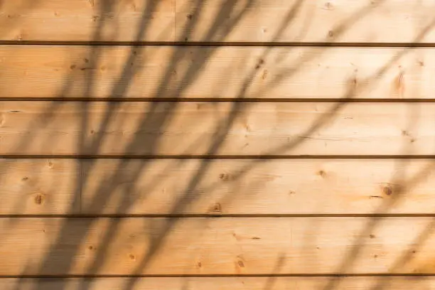 Photo of The facade of the house is made of new horizontal wooden boards. Wooden texture. With sunlight and shadows