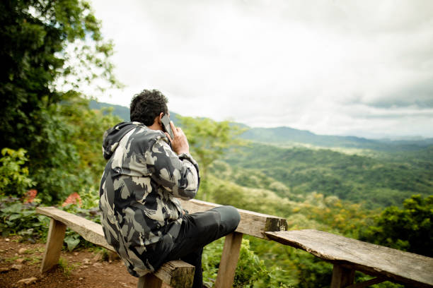 istock rear view of asian man using phone when sitting on the bench with forest in view 1362827714