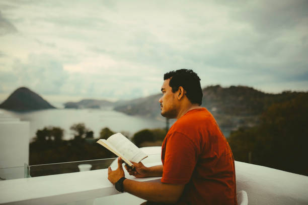 asiático homem lendo livro na varanda do hotel - balcony beach book men - fotografias e filmes do acervo