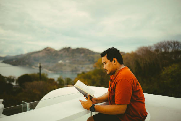 asiático homem lendo livro na varanda do hotel - balcony beach book men - fotografias e filmes do acervo