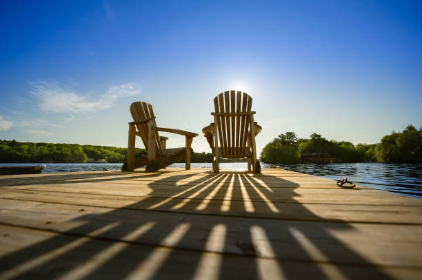 sonnenaufgang auf zwei leeren adirondack-stühlen, die auf einem dock sitzen - landhaus stock-fotos und bilder