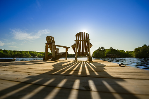 Sunrise on two empty Adirondack chairs sitting on a dock