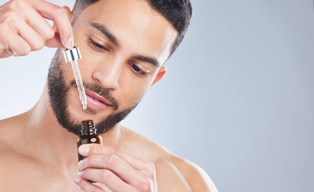 scatto in studio di un bel giovane che applica il siero sul viso su uno sfondo grigio - barba foto e immagini stock