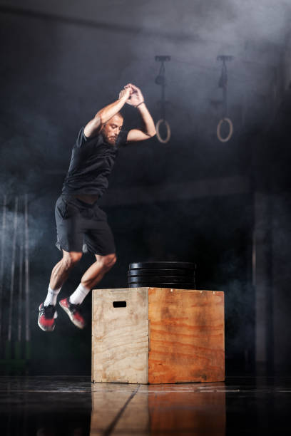 atleta musculoso saltando sobre caja de madera. entrenadora de crossfit en un gimnasio. fondo de humo. - healthy lifestyle men boxing dumbbell fotografías e imágenes de stock