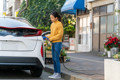 Mid adult woman plugging in an electric car to charge. Okayama, Japan, 2021.