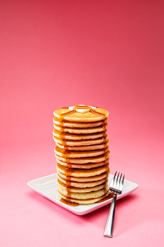 This is a photograph of a large tall stack of pancakes on a pink background