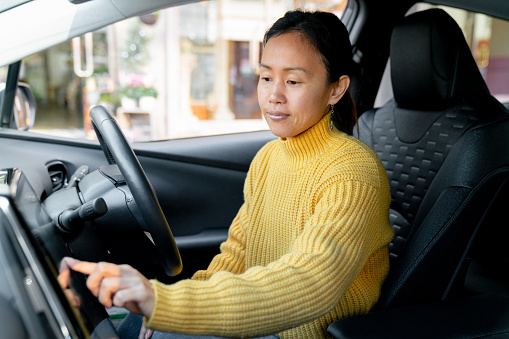 Mid adult woman using touch screen in her electric car. Okayama, Japan. 2021