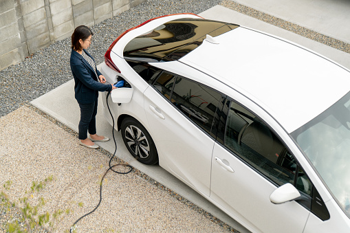 Mid adult woman charging her electric car at home. Okayama, Japan. 2021