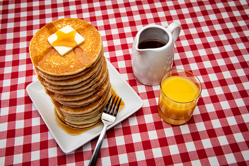 This is a photograph of a large tall stack of pancakes on a checkered table cloth in the studio