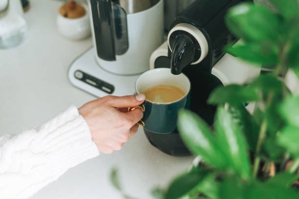 foto ritagliata di giovane donna versa il caffè dalla macchina da caffè in cucina a casa - machine made foto e immagini stock