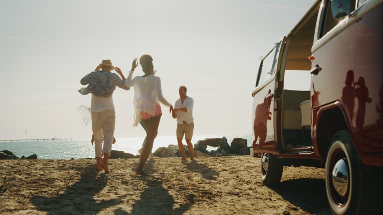 Slow motion of group of young multi-ethnic friends are arrived on a beach near the sea and having fun to go out from minivan in with a sun shining.