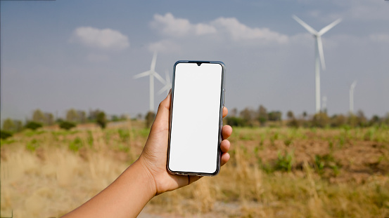 A smartphone with a creative white screen and a field of electric wind turbines in the background.