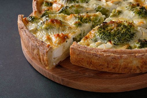 A slice of traditional french open quiche pie with feta cheese and broccoli on a dark green background. Horizontal orientation.
