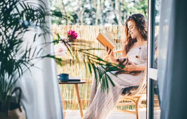 Photo of Young woman reading a book in the balcony.