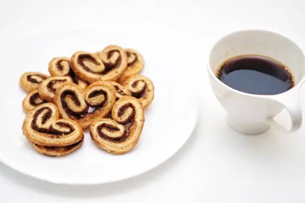 Photo of Cinnamon sugar palmiers on white plate, blurred a cup of hot coffee