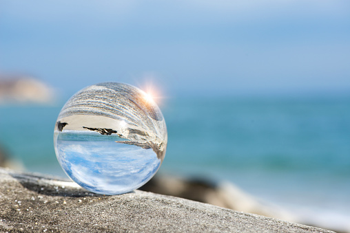 Upside down seascape with blue sky and rocks - reflection in a lens ball - selective focus, space for text