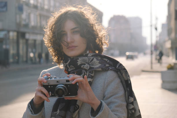 beautiful woman photographer portrait taking photos with a vintage camera in the city - photographer enjoyment elegance old fashioned imagens e fotografias de stock