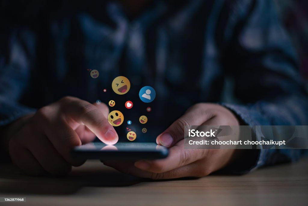 Young man using smartphone sending emojis, diverse positive emoji coming out of mobile phone. Mobile application for chatting, creative image, Social media concept. Social Media Stock Photo