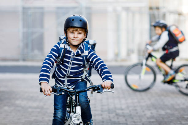 Two school kid boys in safety helmet riding with bike in the city with backpacks. Happy children in colorful clothes biking on bicycles on way to school. Safe way for kids outdoors to school stock photo
