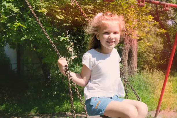 Photo of Happy child girl on swing, summer time. Life Events.  Retro toned, Soft focus effect