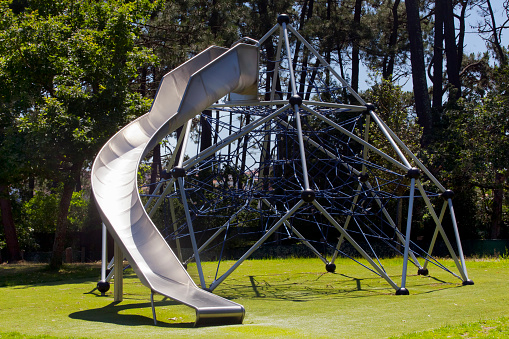 Metal curve sledge part of a children playground, outdoor play equipment, public park , pine  trees in the background. Galicia, Spain