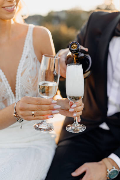 close-up photo of newlyweds hands, men and women hold glasses of champagne or white wine. drink is poured. wedding day romantic evening on rooftop against background of city. - champagne champagne flute wedding glass imagens e fotografias de stock