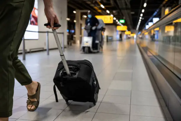 An unrecognisable man pulling a small suitcase behind him while walking through the airport in the Netherlands. The main focus is the suitcase.