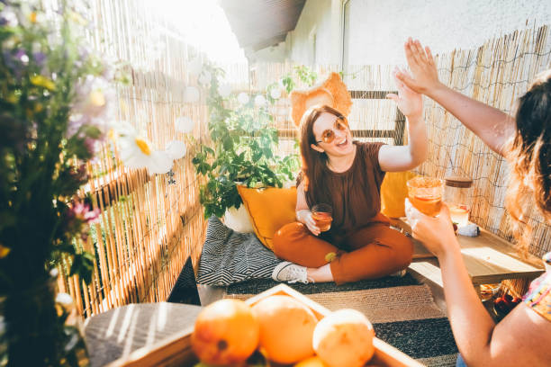 Joyful young woman clinks glasses with delicious cocktails with friend spending time together on decorated terrace on summer day close view. stock photo