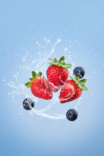 istock Flying strawberry with water splash isolated on blue blackground. Vertical format. Gravity concept. 1362885927