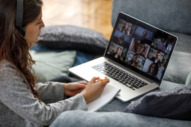 istock Young woman writing class notes during group video call with professor and classmates 1362892010