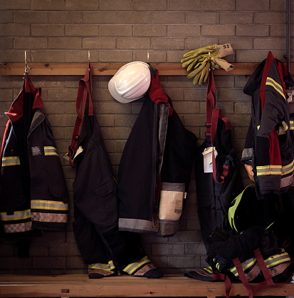 Firefighting gear including helmets, gloves, jacket and trousers among other equipment in fire station.