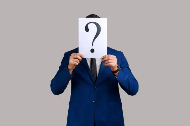 Photo of Unknown man hiding face behind white paper with question mark, finding solution, asking for advice.