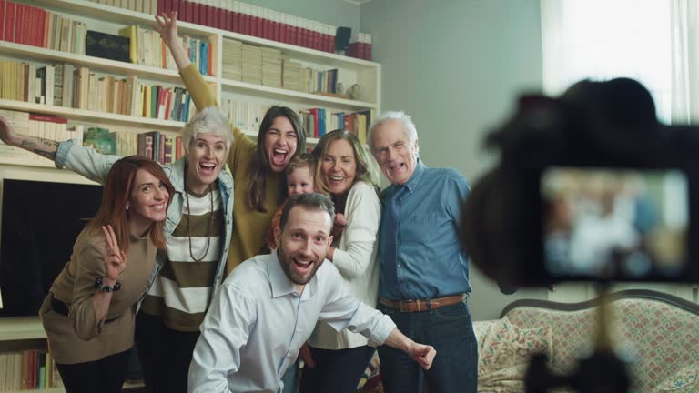 Cinematic shot of happy family members  making family photo portrait with photo camera on tripod with timer during a reunion party at home. Concept of memories, happiness, life, emotion, generations.