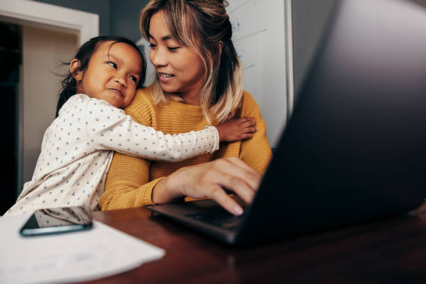 Little girl embracing her mom in her home office Adorable little girl embracing her mom in her home office. Working mom smiling at her daughter while typing an email on a laptop. Self-employed mother of one working remotely. working at home with children stock pictures, royalty-free photos & images