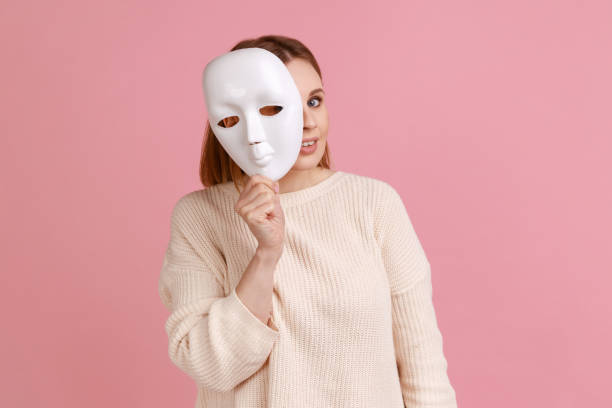 blond woman holding white mask, peeking, looking at camera, pretending to be another person. - spy secrecy top secret mystery imagens e fotografias de stock