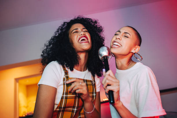 mejores amigos cantando en un micrófono en la noche de karaoke - feliz mujer con micrófono de música karaoke en club nocturno fotografías e imágenes de stock