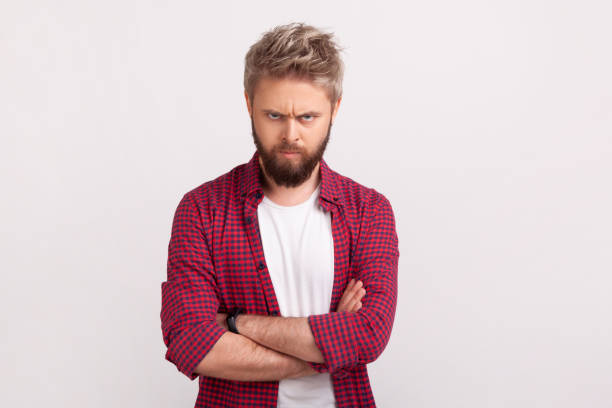Portrait of aggressive bossy bearded man with grumpy face and folded arms angrily looking into camera, bad mood