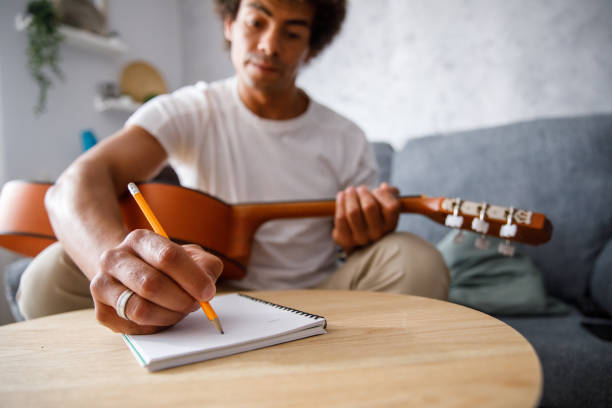 istock Young man composing a song for acoustic guitar, writing chords in a notebook 1362895061
