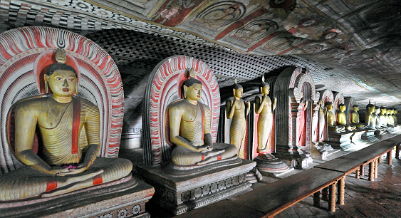Row of Buddha effigies, Dambulla Cave Complex, Matale District, Central Province, Sri Lanka. This network of underground caves is remarkable for its numerous carved sculptures and paintings dedicated to the god Buddha and his life in various positions, reclining, standing and seated that date from the first century and is the most significant archaeological site in Sri Lanka.