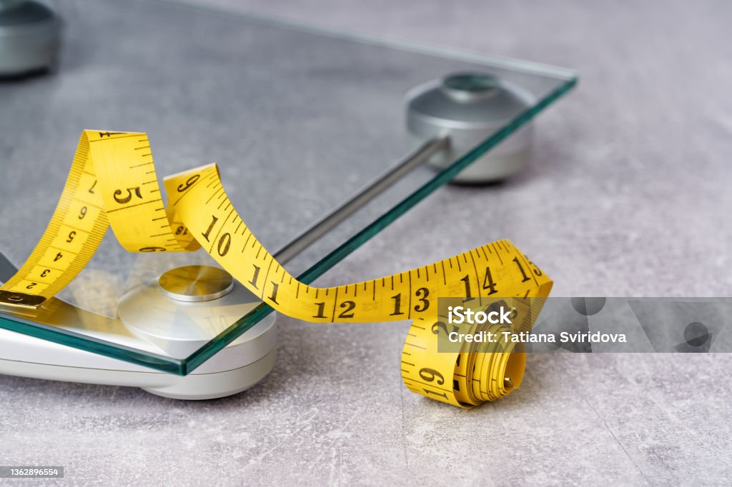 yellow tape measure on glass bathroom scale yellow tape measure on top of glass bathroom weighing scale on blue. Front view copy space. Healthy lifestyle, weight losing management and hydration concept banner Weight Scale Stock Photo