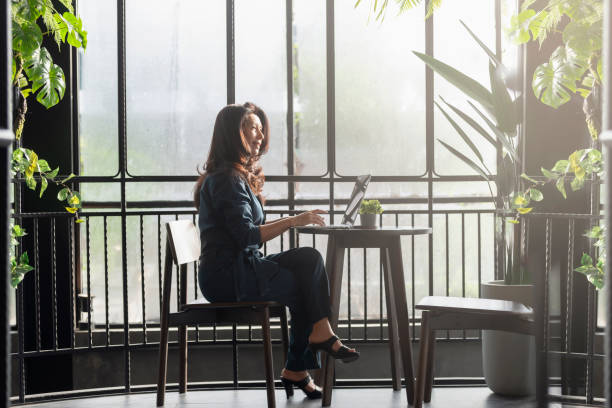 オフィスやカフェのインテリアでラップトップコンピュータで働くアジアの女性を考えます。クライアントに対する笑顔の女性タイピング応答は、オンラインだけでラップトップ上でリモー� - relaxation success luxury women ストックフォトと画像