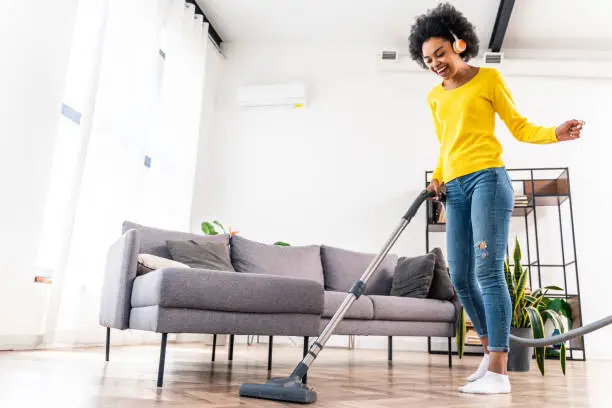 Photo of Happy afro woman having fun while cleaning home and listening music