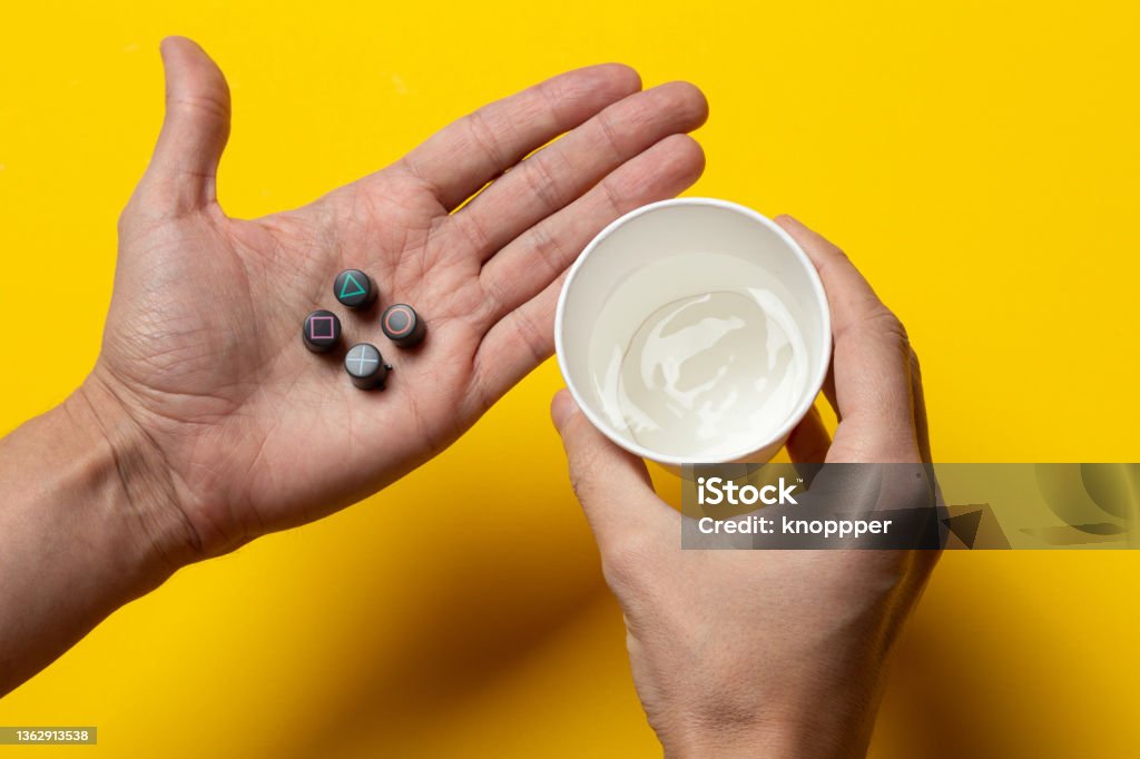 Playstation buttons on the palm and a glass of water Playing games to escape reality, Video game addiction Gamification Stock Photo