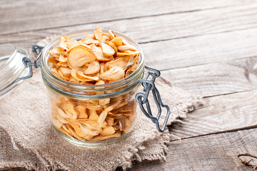 Dry chopped garlic slices in a glass jar on a wooden table, empty space for text