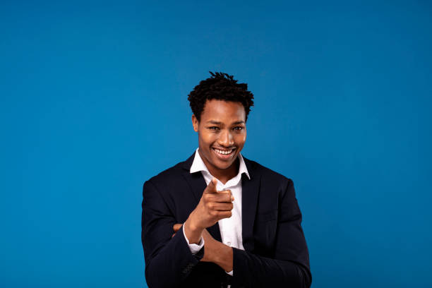 istock Smiling successful african businessman posing over blue studio background, pointing to the camera. 1362921086