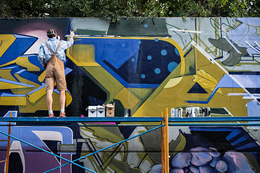 Graffiti street artist is painting on wall outdoor.