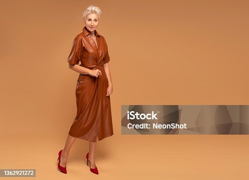istock Beautiful blonde middle aged woman with short hairstyle posing in brown medium dress. Fashion photo. Elegant businesswoman. Full photo 1362921272