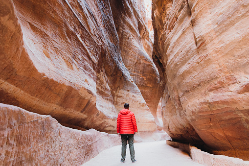 Young woman explorer in red jacket hiking in the beautiful pink canyon in the old town of Petra in the Middle East